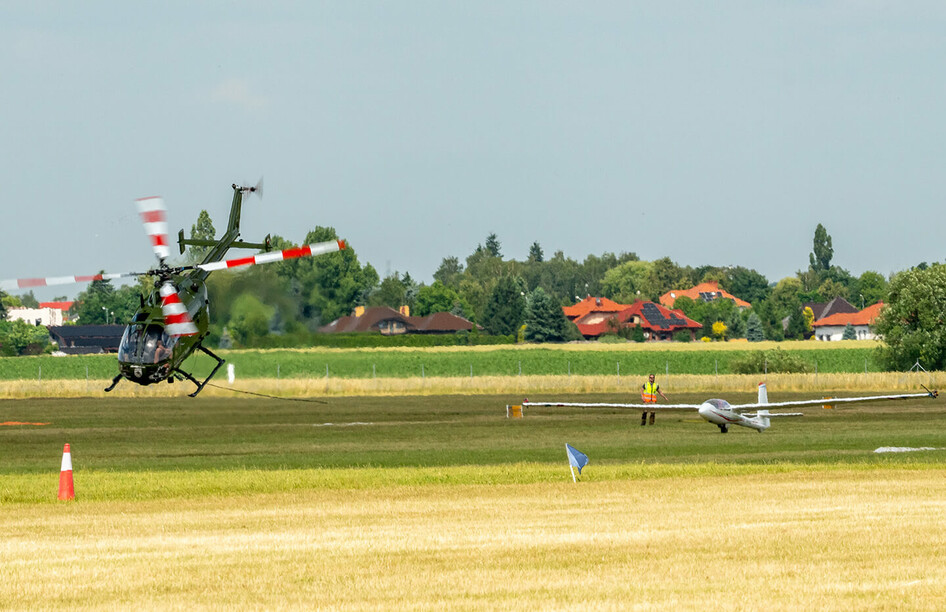 Helikopter hebt Segelflugzeug SZD-59-1 Acro vom Flugplatz ab.